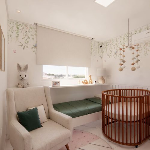 Quarto de bebê em tons claros, com papel de parede de folhagens, poltrona de amamentação e berço redondo de madeira